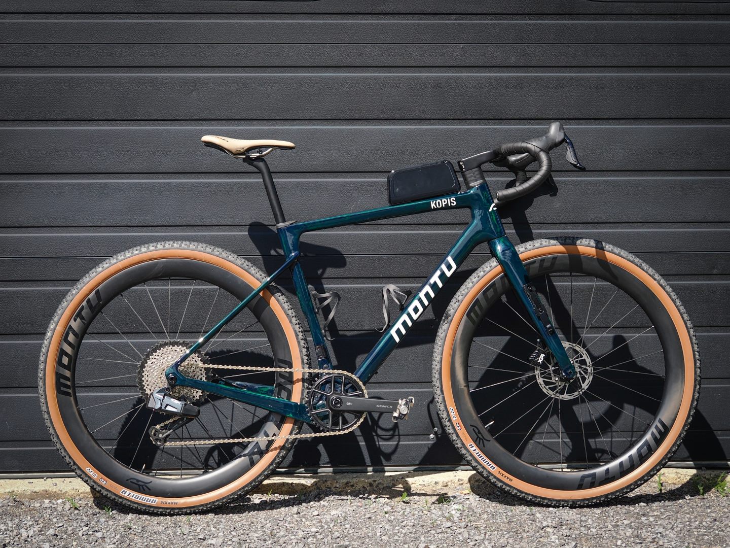 Montu Kopis gravel bike in translucent emerald green, full side profile on tan-wall Montu wheels