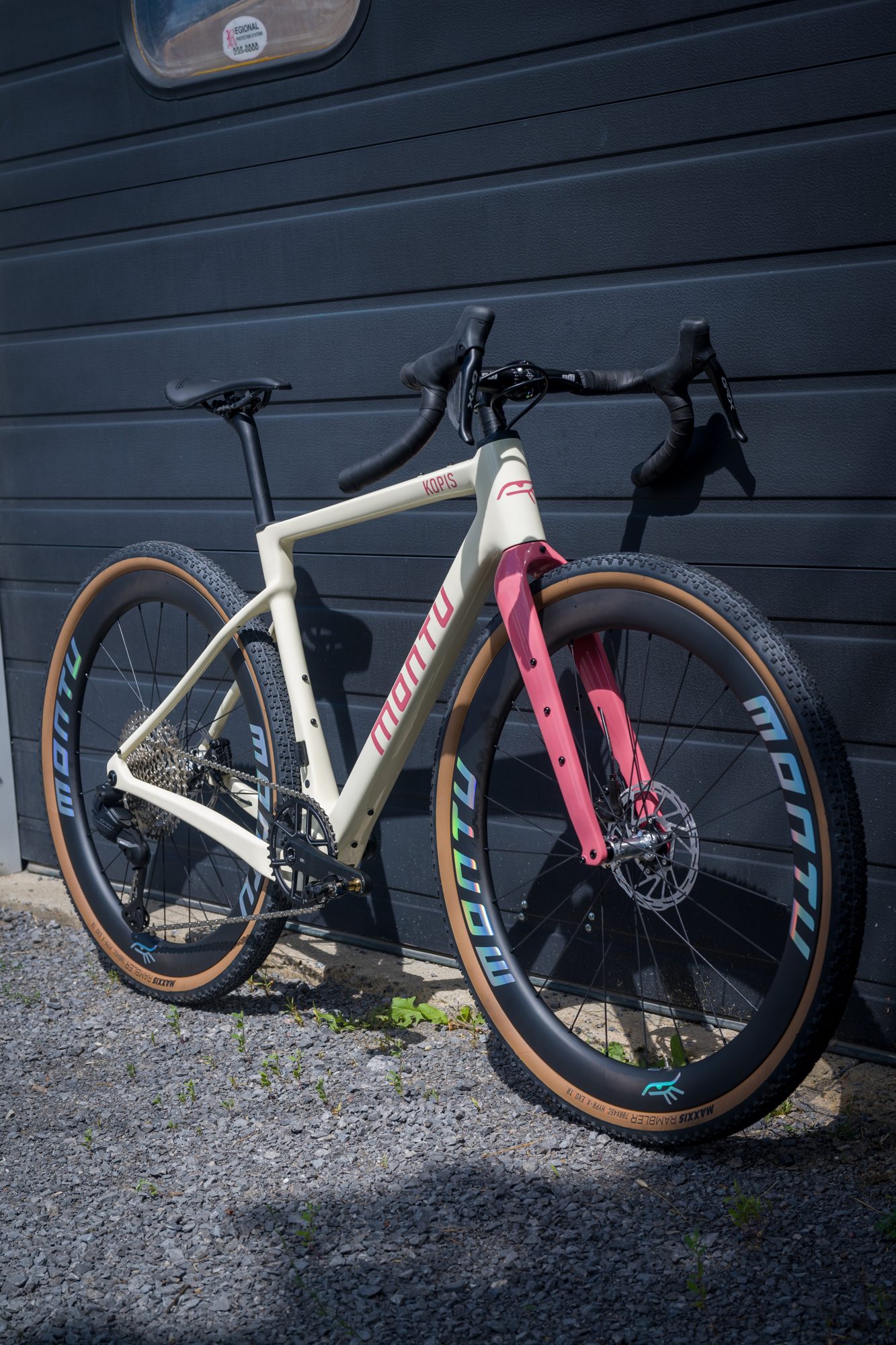 Montu Kopis in cream with a pink fork, leaning against a dark garage door